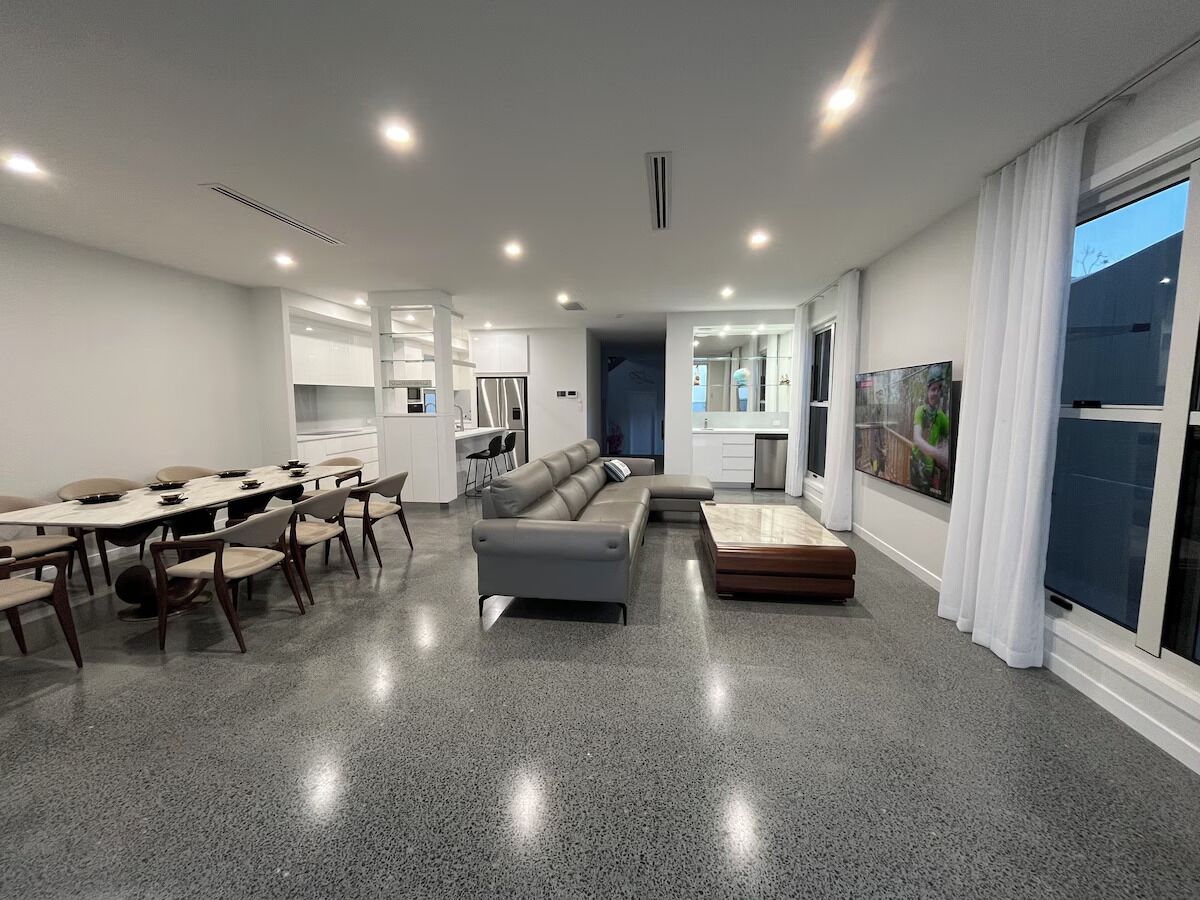 A modern living room with a dining area, a sofa, and a kitchen in the background.