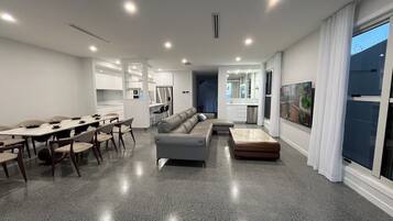 A modern living room with a dining area, a sofa, and a kitchen in the background.