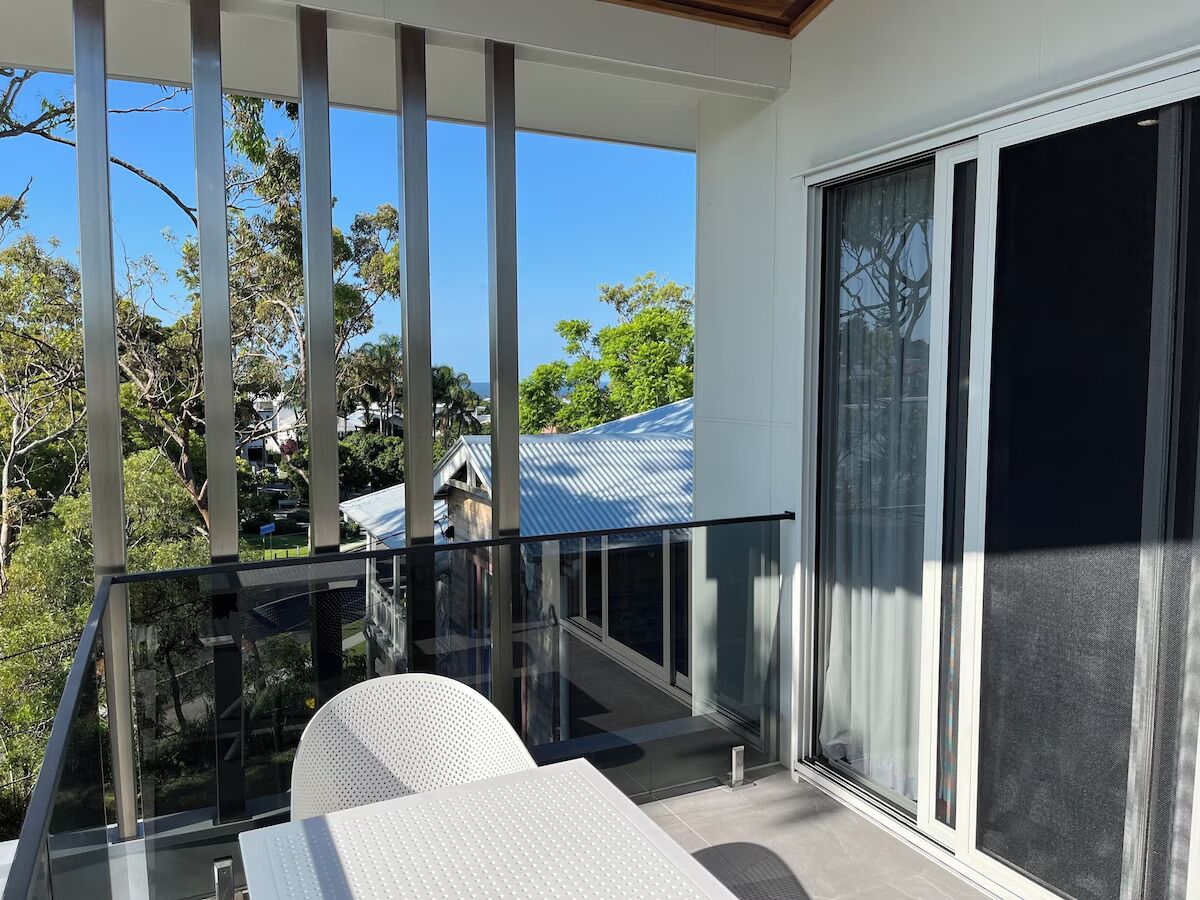 A balcony with a glass railing, a white chair, and a view of a house with a blue roof.