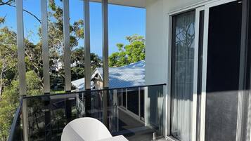 A balcony with a glass railing, a white chair, and a view of a house with a blue roof.