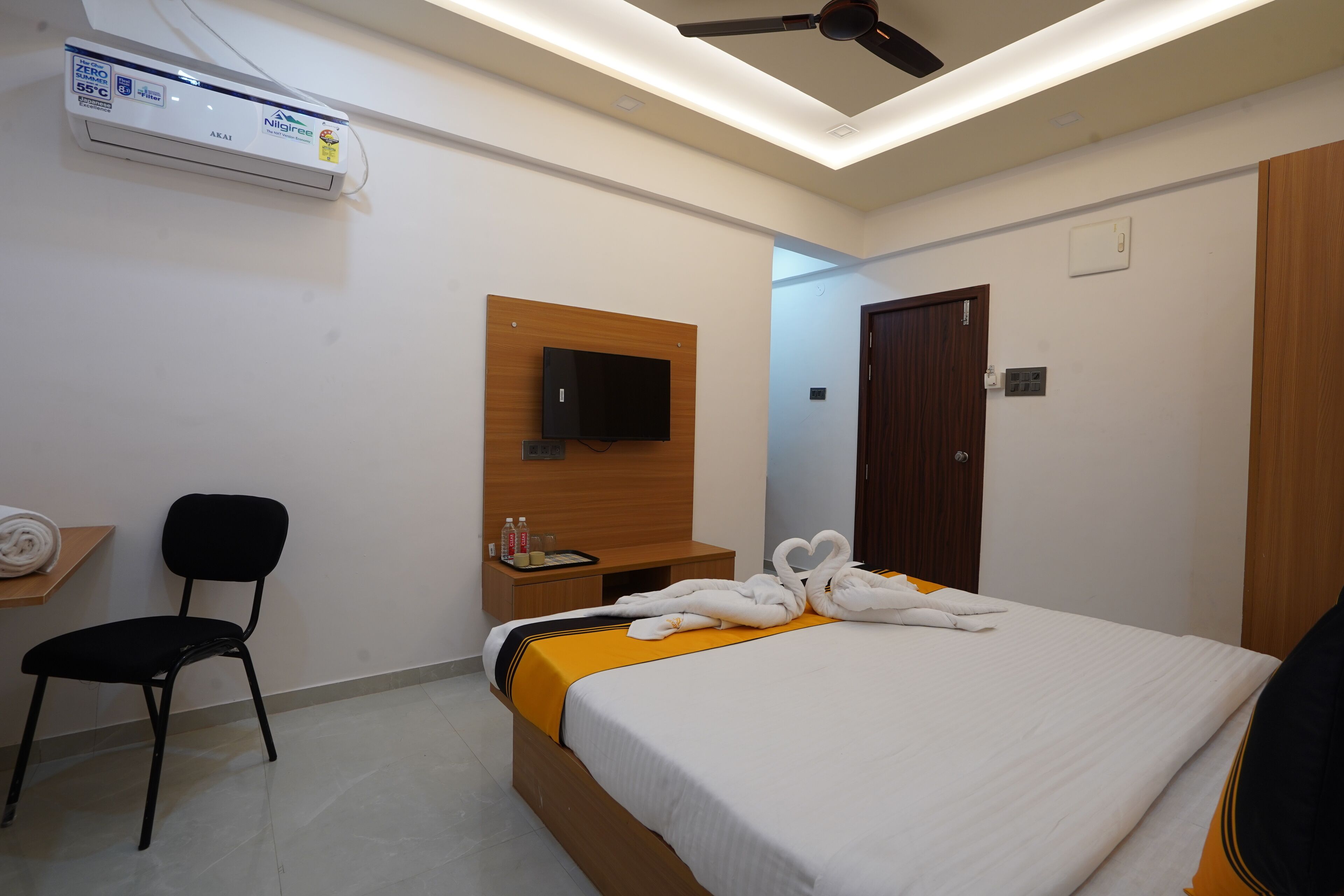 Une chambre d’hôtel comprenant un lit, un téléviseur à écran plat fixé sur un panneau en bois, un ventilateur de plafond, un appareil de climatisation, une chaise et une armoire en bois.