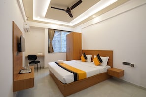 Una habitación de hotel moderna con una cama grande, un escritorio con silla, un televisor y un ventilador de techo.