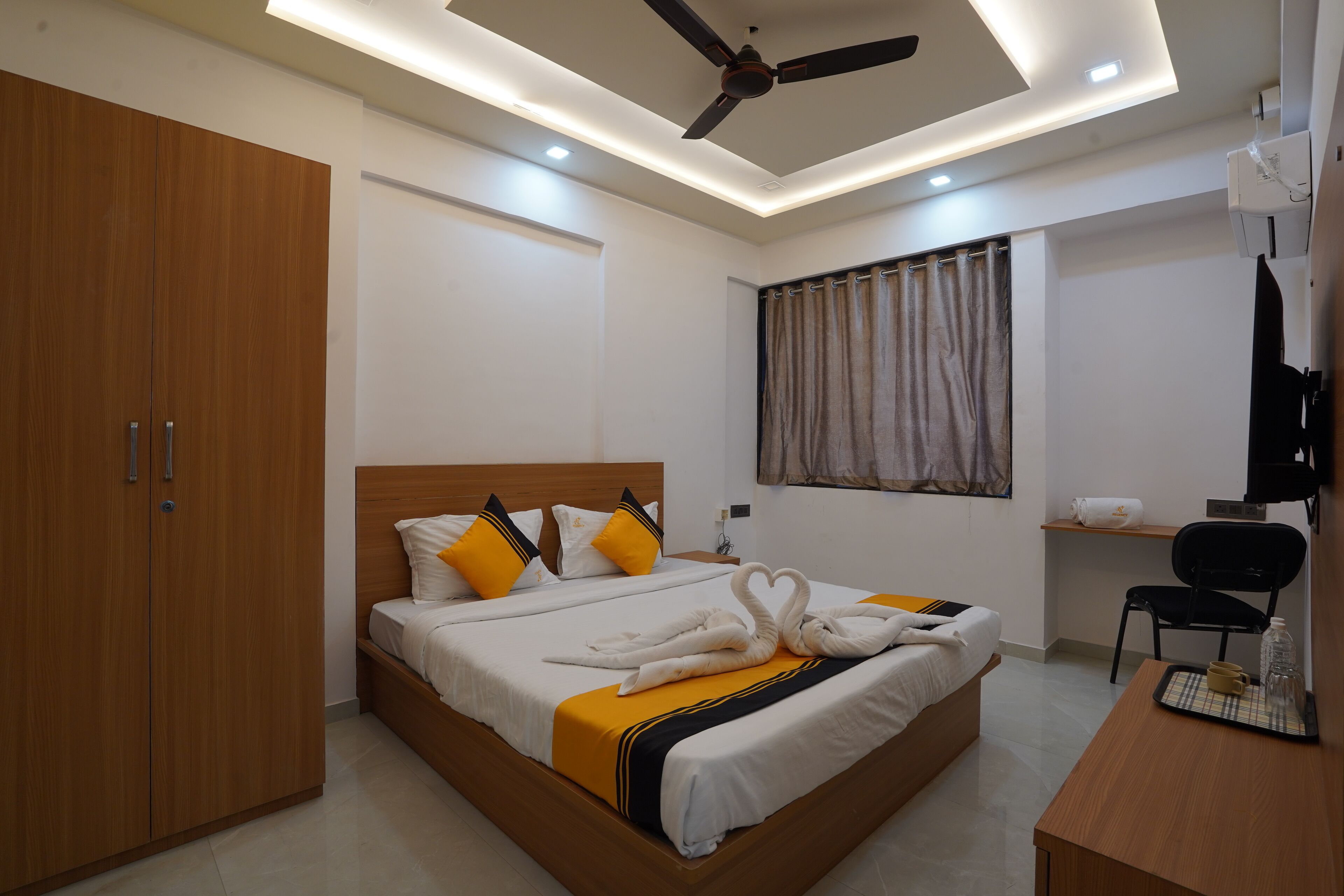 Una habitación de hotel con cama, escritorio, silla, armario y ventilador de techo.