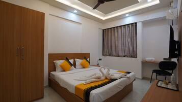 Una habitación de hotel con cama, escritorio, silla, armario y ventilador de techo.