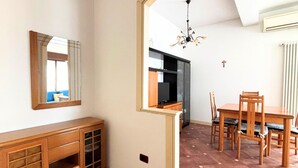 Ein Zimmer mit Holzschrank, Esstisch mit Stühlen, einer Chandelierleuchtre und einer Küchenzeile.