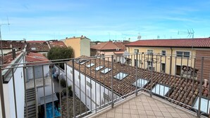 Eine Dachterrasse mit Fliesenboden, Metallgeländer und Blick auf die Nachbargebäude.