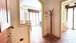 Ein Innenbereich mit einem Holztür, einem Kleiderständer und einem Fliesenboden, der zu einem Essbereich mit Stühlen und einem Tisch führt.