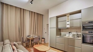 Eine moderne Küche mit Edelstahlgeräten, ein Essbereich mit Tisch und Stühlen sowie ein Wohnbereich mit Sofa und Hocker.