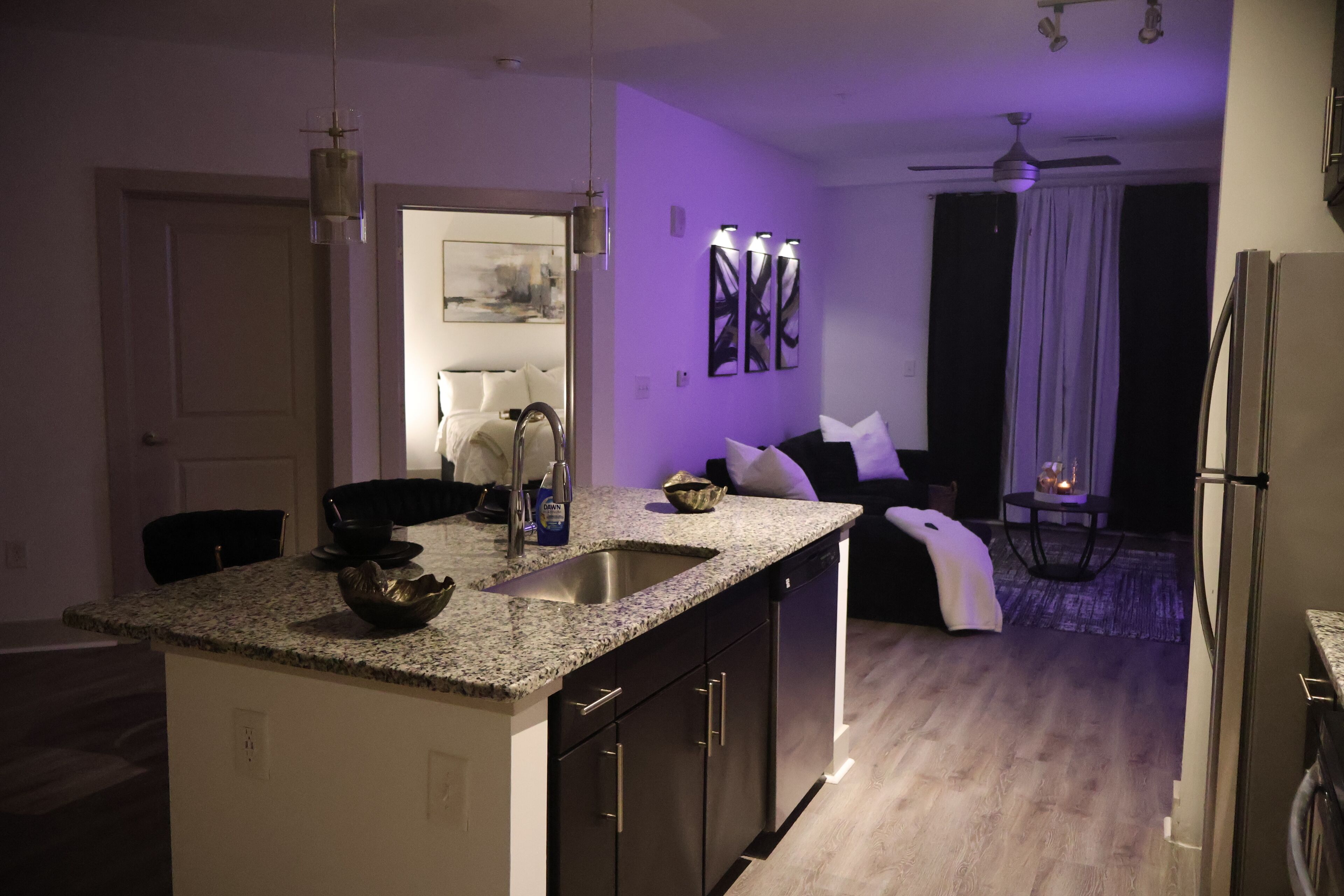 A modern kitchen with granite countertops, a built-in dishwasher, and a dining area with a black chair and a white table.