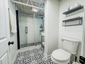A bathroom with a white toilet, a shower enclosure, and patterned floor tiles. - Spacious 3-bedroom Comfort Urban Chicago loft house (Chicago)