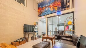 Een ruime woonkamer met een grote flatscreen-tv, lederen meubels en een stadsgezicht muurschildering.