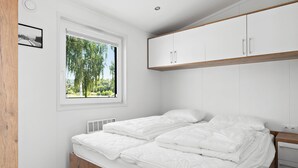 Une chambre à coucher avec un lit, une fenêtre donnant sur des arbres, des armoires blanches et une tête de lit en bois.