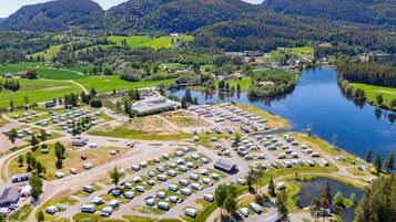 Vista aérea de un camping con vehículos recreativos estacionados en filas ordenadas, un lago y colinas verdes circundantes.