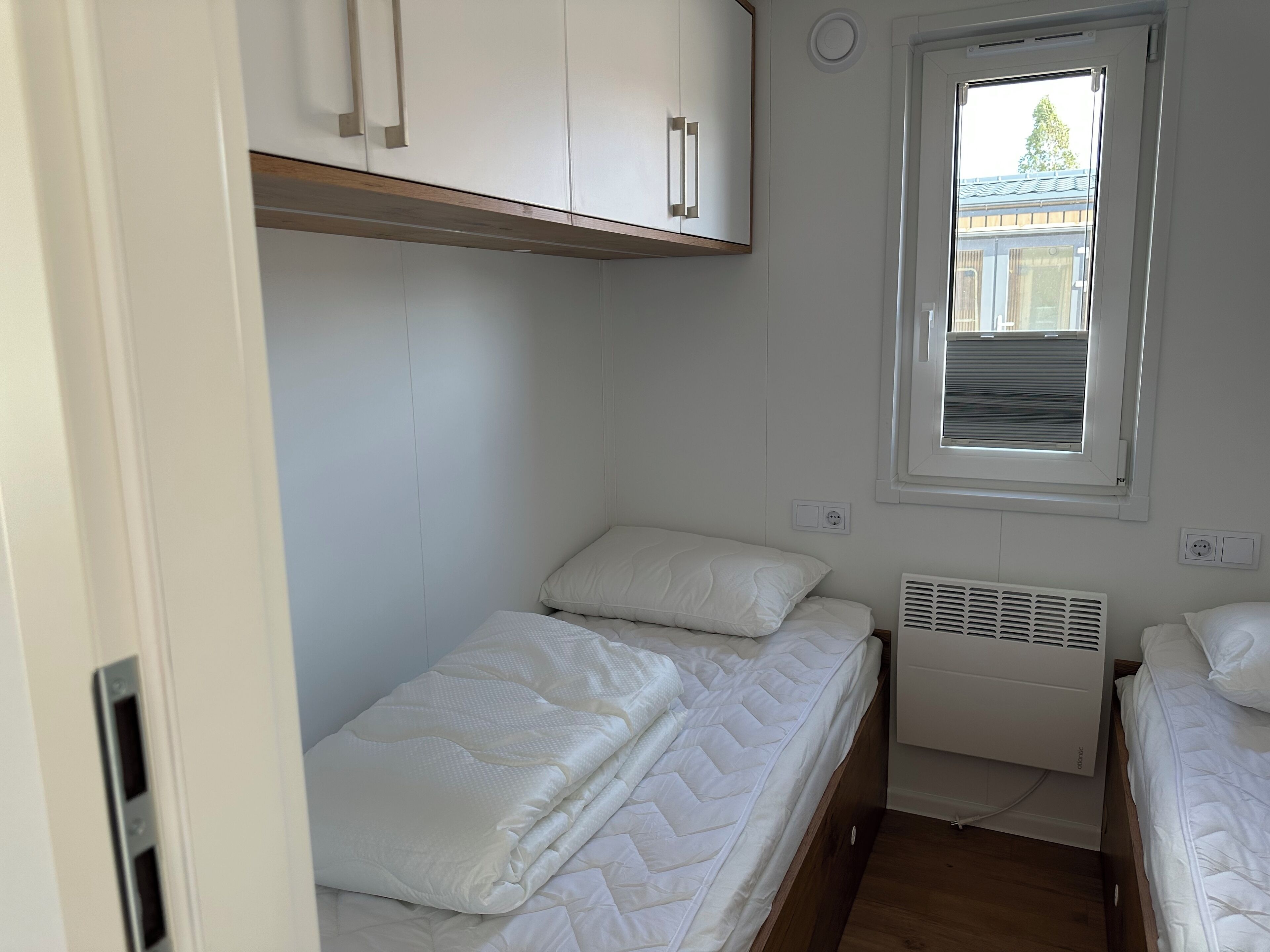A small, clean room with a bunk bed, a window with blinds, and a white radiator.
