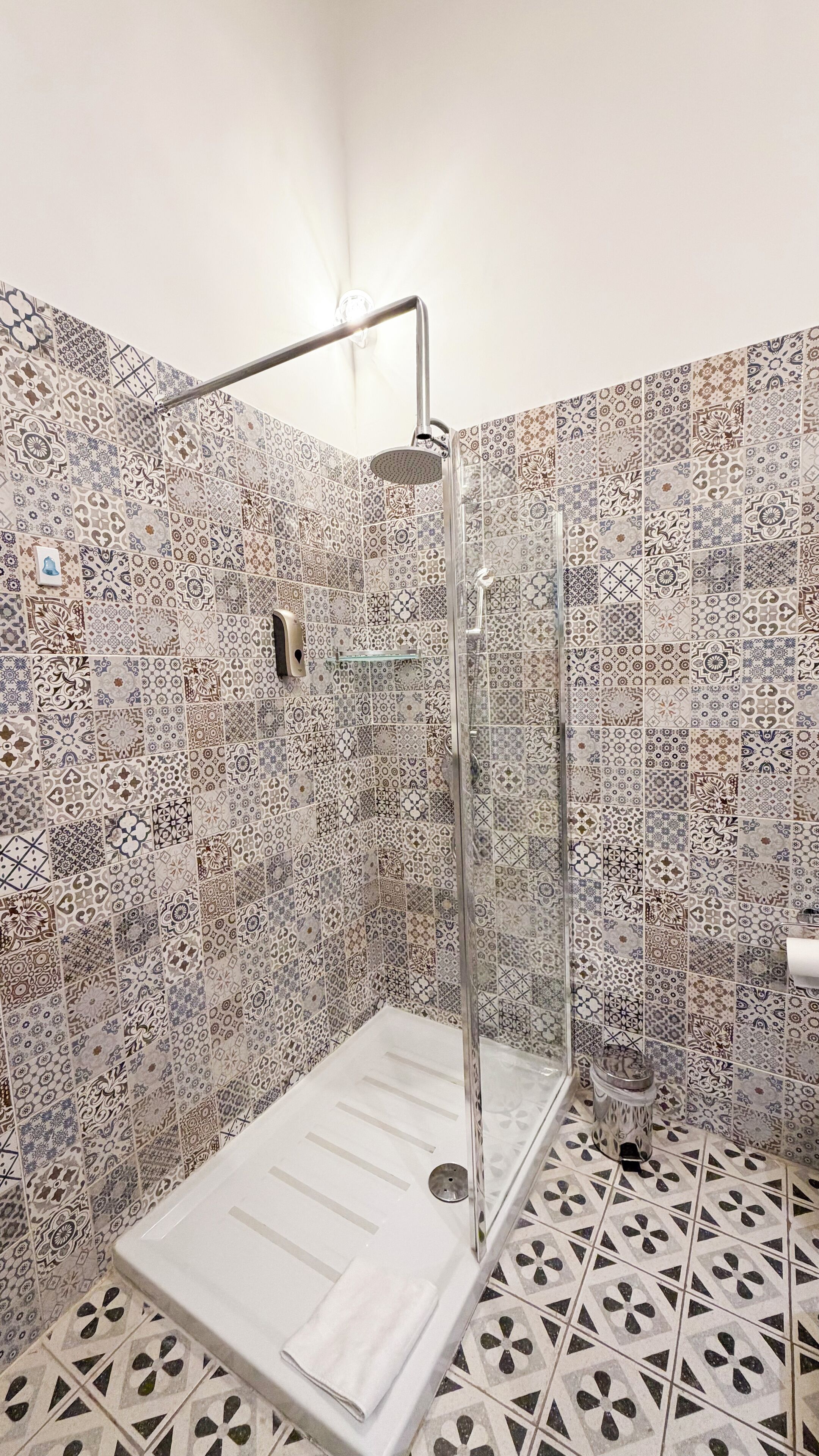 A shower area with a glass door, a metal showerhead, and a tiled wall with a complex pattern.