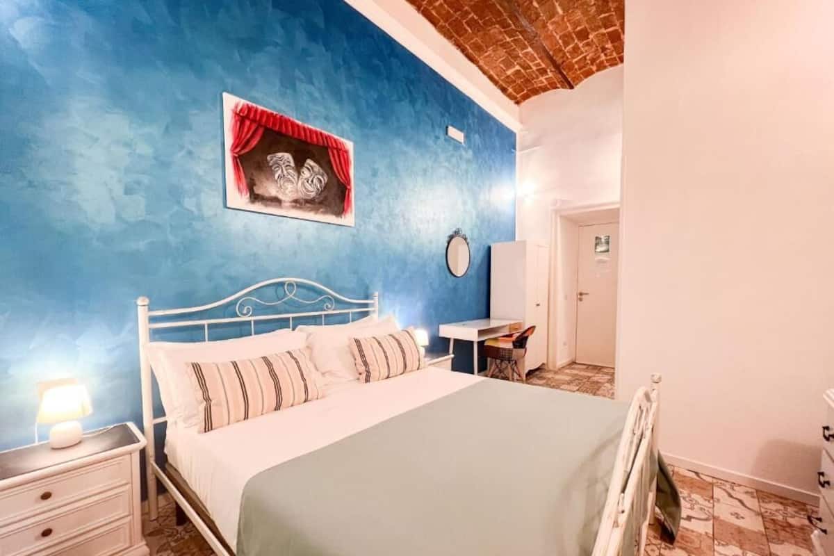 A bedroom with a bed, nightstand, and a wall-mounted picture.