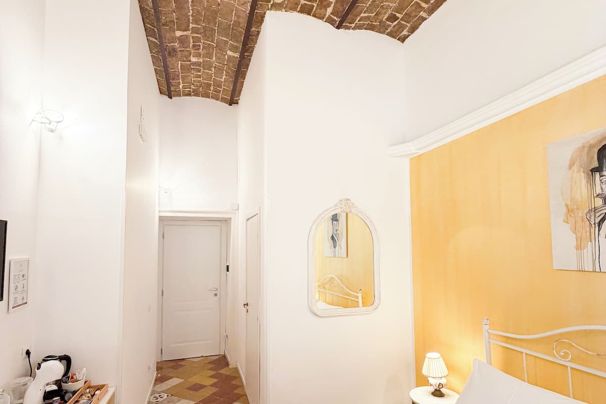 A room with a bed, a desk, and a chair. There is a door leading to another room.