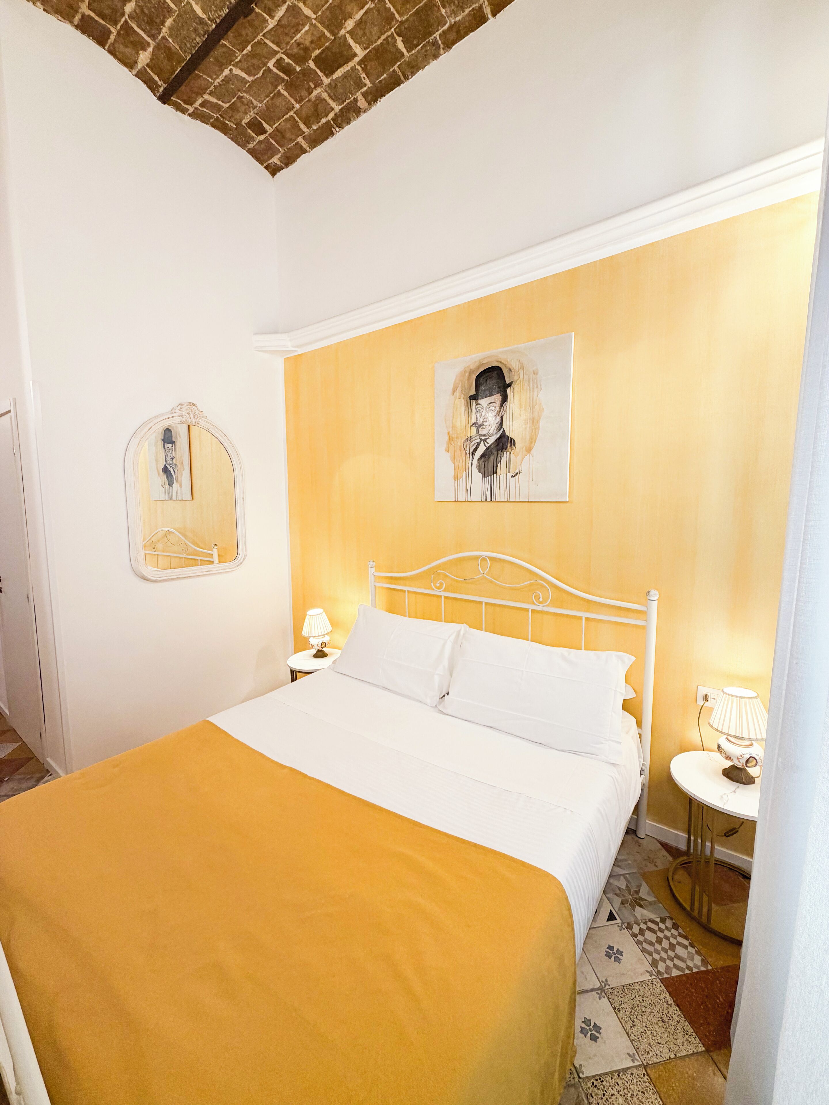 Une chambre d’hôtel avec un lit, une table de chevet, une lampe, un miroir et un tableau au mur.