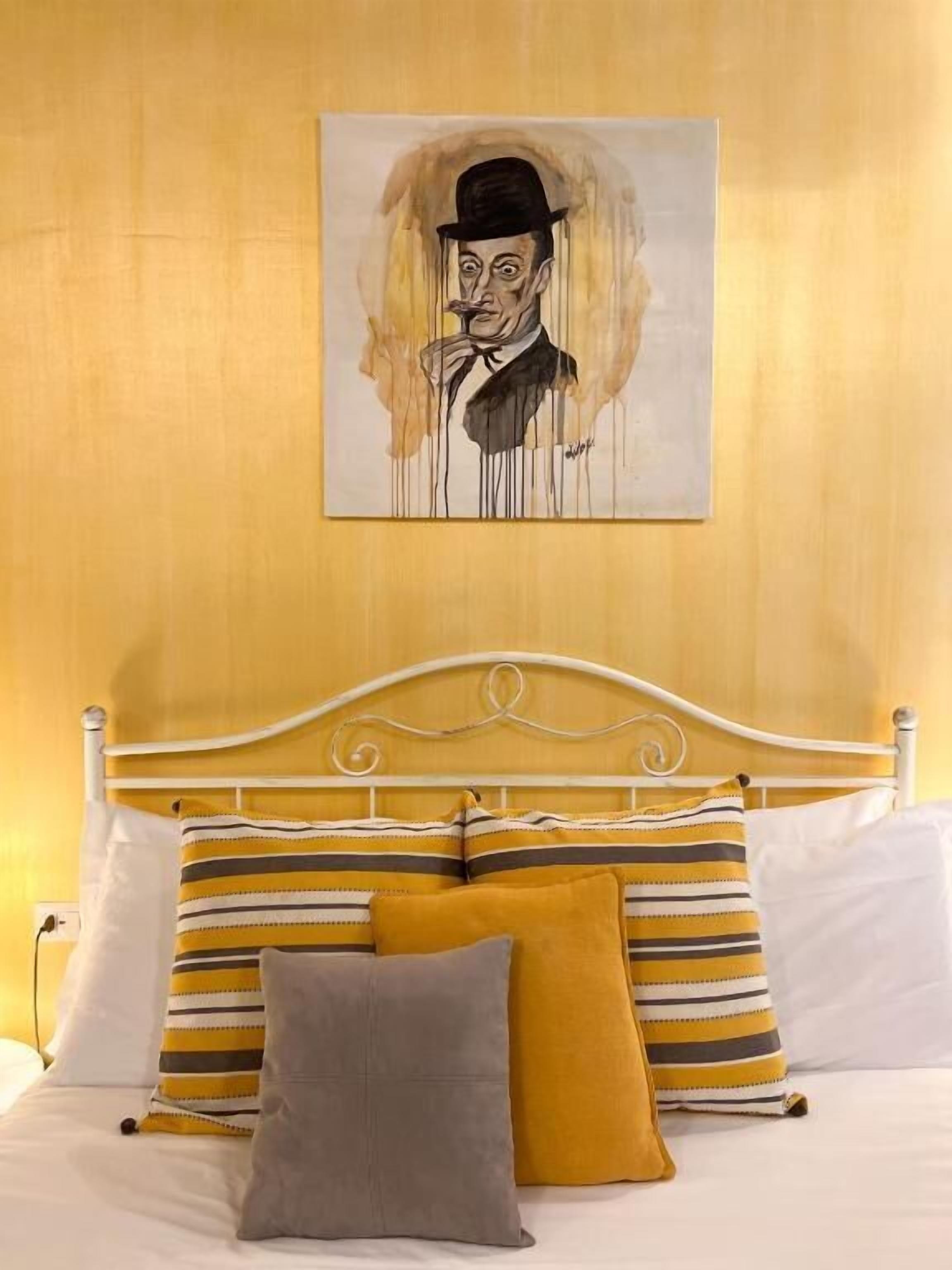 A bed with striped pillows and a painting of a man on the wall.