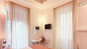 Une chambre d’hôtel avec un lit, un bureau, une chaise, une télévision et une fenêtre avec des rideaux.