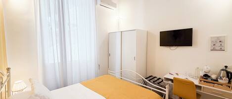Una habitación de hotel con cama, escritorio, silla, televisor y armario.