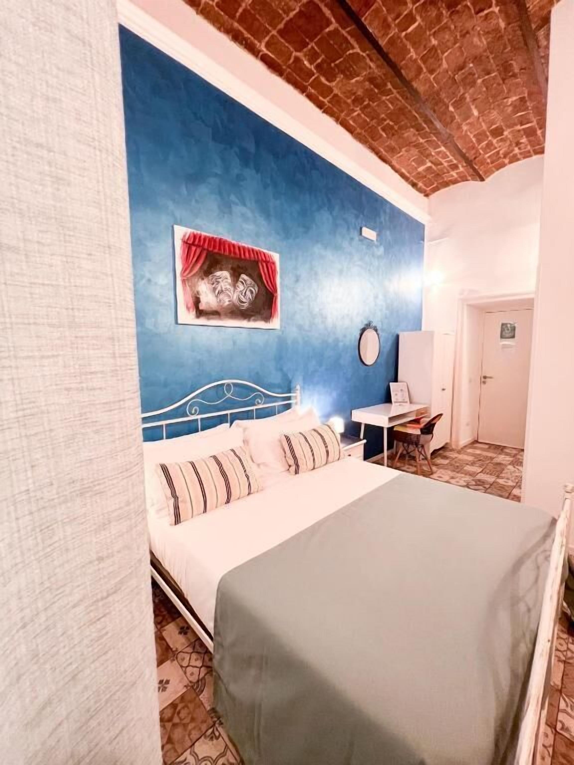 Ein Schlafzimmer mit einem Bett, einem Schreibtisch, einem Stuhl, einer Wand mit einer Theatermaske und einer Tür.