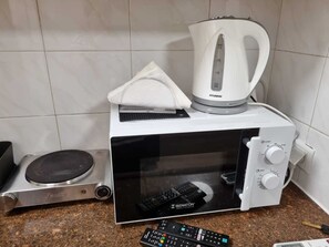 Eine kompakte Mikrowelle zusammen mit einem Wasserkocher und einer Fernbedienung auf einer Arbeitsplatte aus Granit.