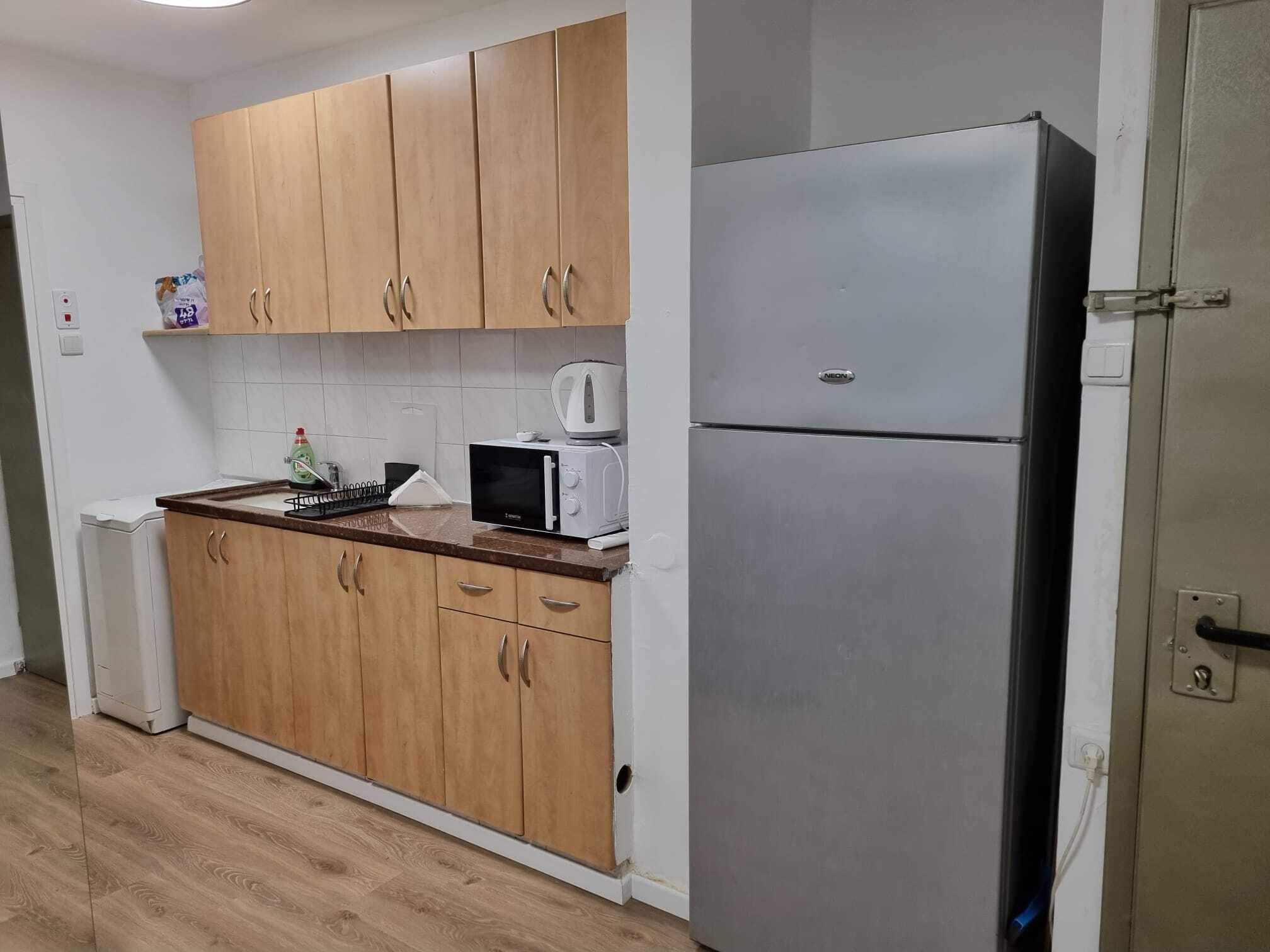 A compact kitchen with wooden cabinets, a white refrigerator, a microwave, and a kettle.