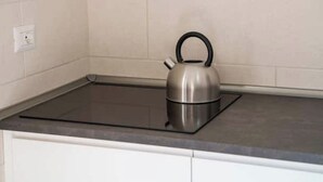 A stainless steel kettle on a black induction cooktop in a kitchen with white cabinets and a light-colored backsplash. - Apartment with Panoramic Sea View in the Heart of Olbia (Olbia)