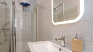 A modern bathroom with a glass-enclosed shower, a white sink with a wooden soap dispenser, and a mirror with a lighted frame. - Apartment with Panoramic Sea View in the Heart of Olbia (Olbia)