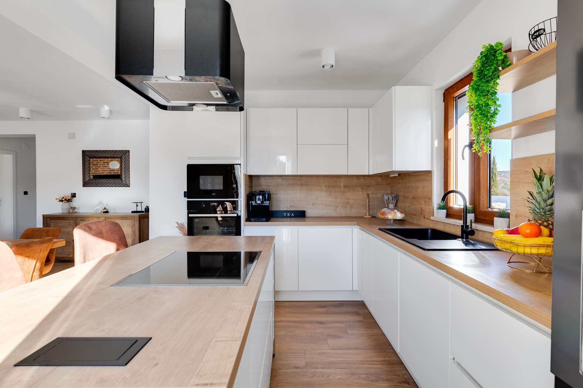 Une cuisine moderne avec des meubles blancs, un plan de travail en bois et un four encastré.