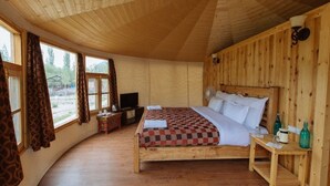 A wooden room with a bed, a TV, and a window with curtains. - Nubra Sarai (Hunder)