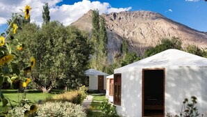 A row of white yurts with wooden doors, set in a lush garden with a mountain in the background. - Nubra Sarai (Hunder)