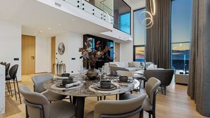 Un'area pranzo moderna con un tavolo rotondo apparecchiato per quattro persone, circondato da sedie. Un'ampia finestra offre vista sulla città.