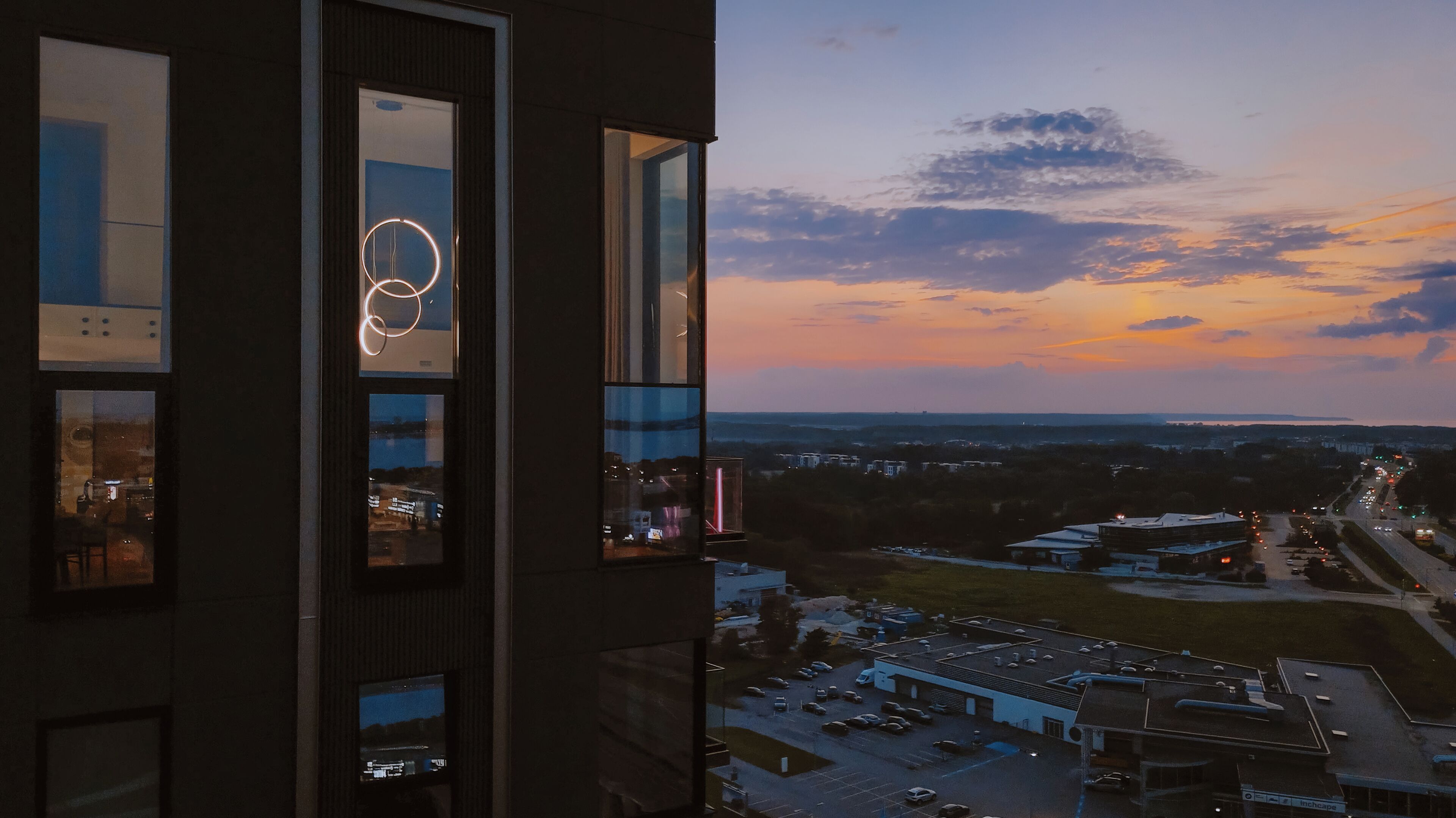 A high-rise building with multiple windows, a view of a parking lot, and a sunset sky.