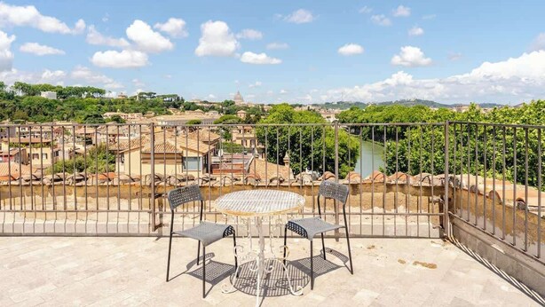 Eine Terrasse mit einem runden Tisch und zwei Stühlen mit Blick auf eine Stadtlandschaft aus Gebäuden und Grünflächen.
