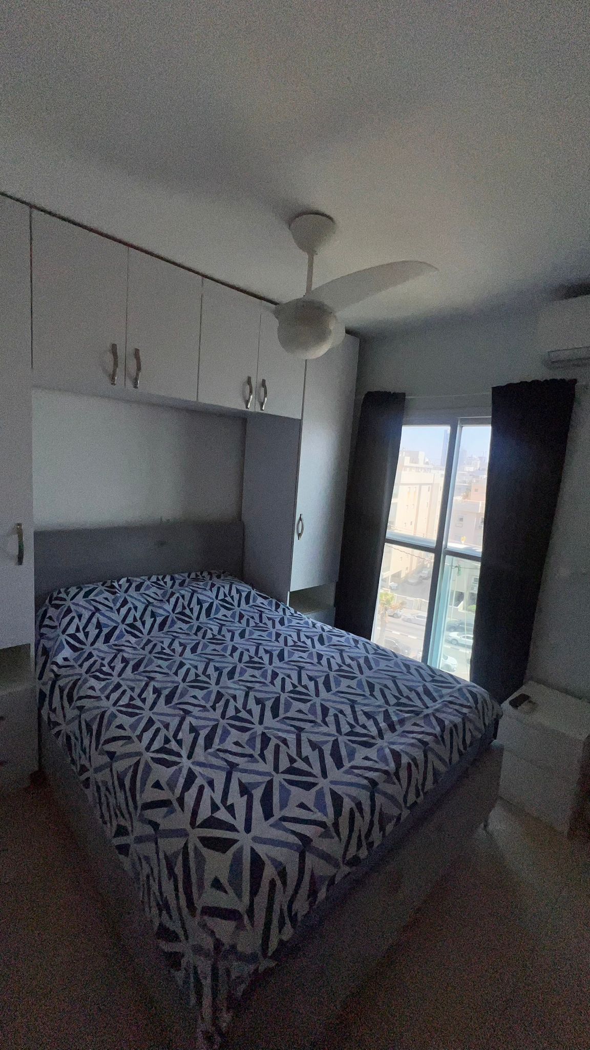 Une chambre à coucher avec un lit, un ventilateur de plafond et une fenêtre avec des rideaux.