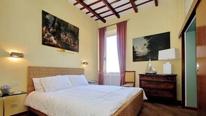 A bedroom with a large bed, two wall-mounted lamps, a wooden ceiling, and two paintings. - Luxury Trastevere apartment (Roma)