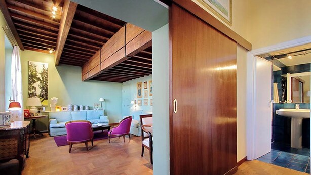 A spacious living area with a wooden ceiling, a large sliding door leading to a bathroom, and a herringbone-patterned floor. - Luxury Trastevere apartment (Roma)