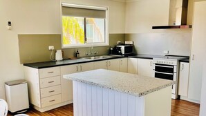 Een moderne keuken met een centraal eiland, houten vloeren en een raam dat voor natuurlijk licht zorgt.