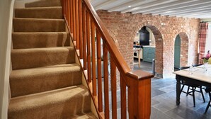 Eine Treppe mit Teppichstufen und Holzbalken, die zu einem Raum mit Backsteinwand und rundbogigem Durchgang führt.