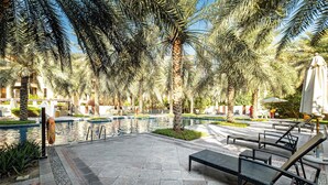 Zona de piscina con sillones de descanso, palmeras y cielo despejado.