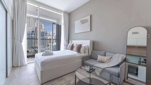 A modern hotel room with a large bed, a sofa, a glass coffee table, and a view of the cityscape. - StayShort - Studio in Marina that Sleeps 3 with a Perfect City View (Dubai Marina)