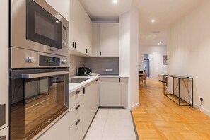 Eine moderne Küche mit integrierten Geräten, ein Essbereich mit Tisch und Stühlen sowie ein Flur, der in einen Wohnbereich führt.