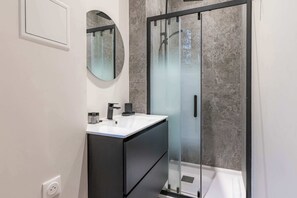 A modern bathroom with a glass-enclosed shower, a white sink, and a dark cabinet. - Charming - Air-conditioned and Terrace (Paris)