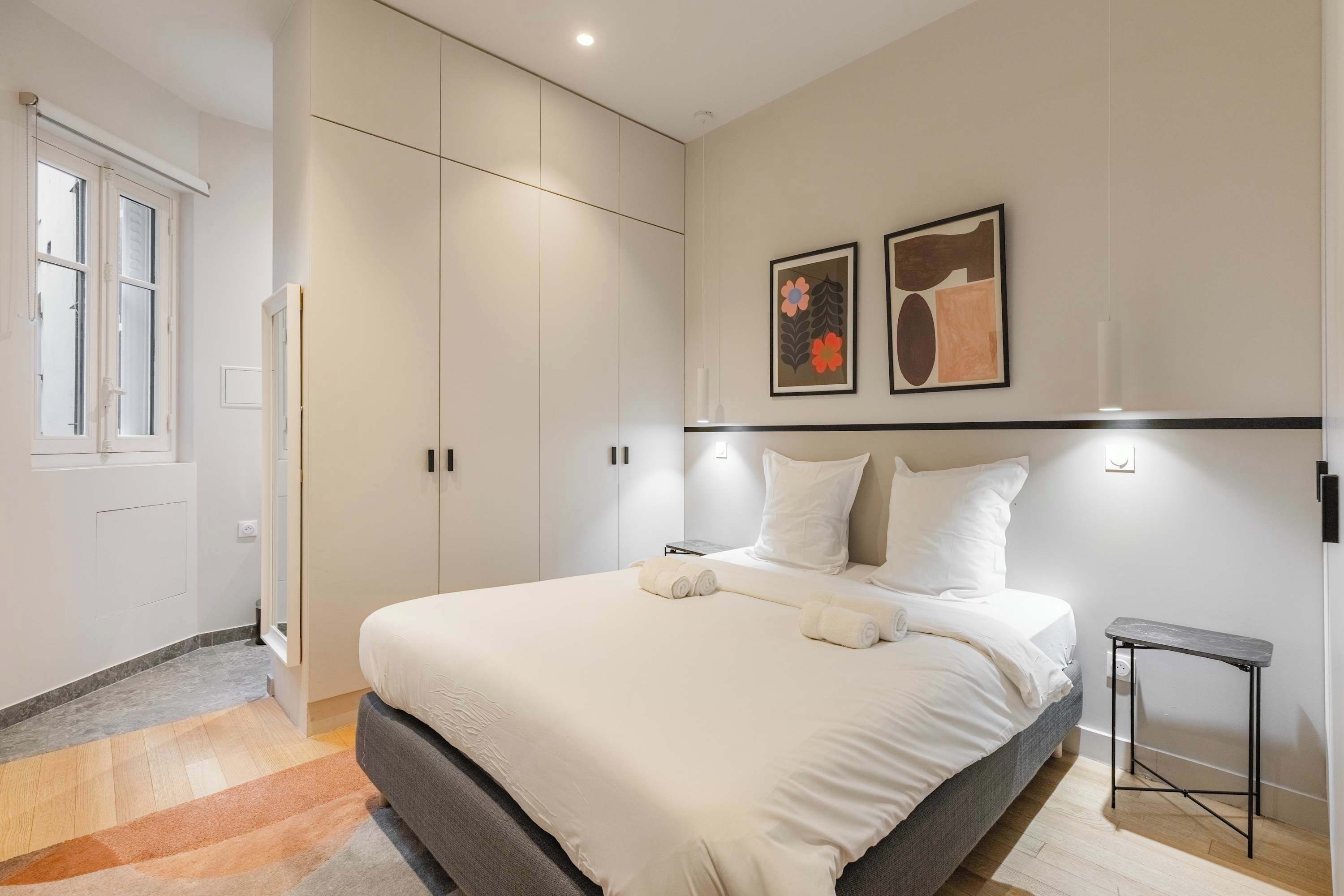 A modern bedroom with a large bed, a wardrobe, and two framed artworks on the wall.