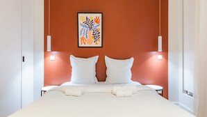 Ein Hotelzimmer mit einem großen Bett, weißer Bettwäsche, zwei weißen Kissen, einem gerahmten Kunstwerk an der Wand und Nachttischlampen.
