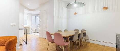 Un espace de salle à manger moderne avec une table et des chaises en bois, un luminaire suspendu et une vue sur une autre pièce.