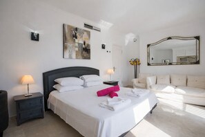 A hotel room with a large bed, a bedside table with a lamp, a sofa, a mirror, and artwork on the wall. - Oceanland, Villa 5StarsHome Mallorca (Calvià)