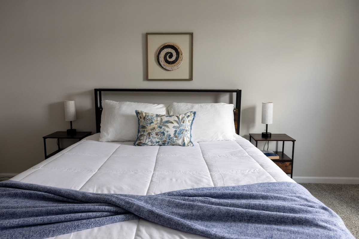 A neatly made bed with a blue blanket, two bedside lamps, and a framed wall decoration.